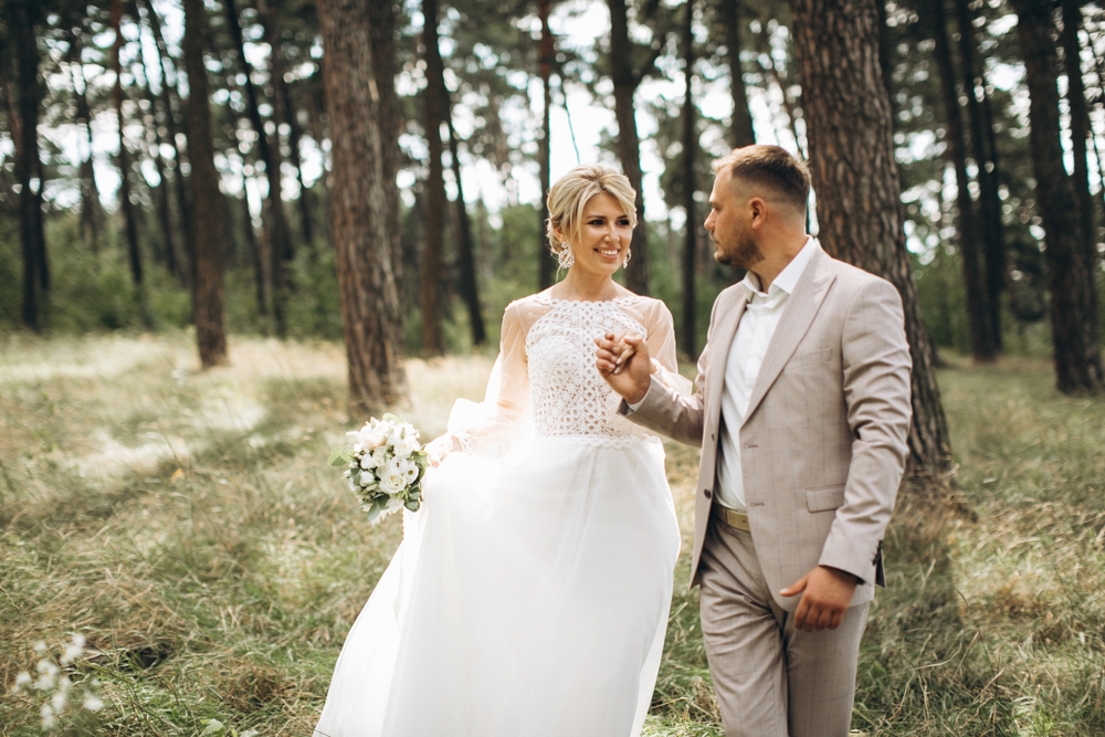 bride and groom walk hand in hand through a pine forest