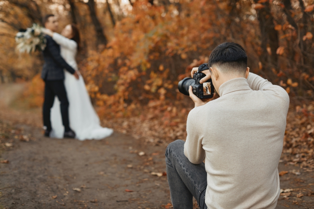 Wedding photographer taking photos of a bride and groom in autumn