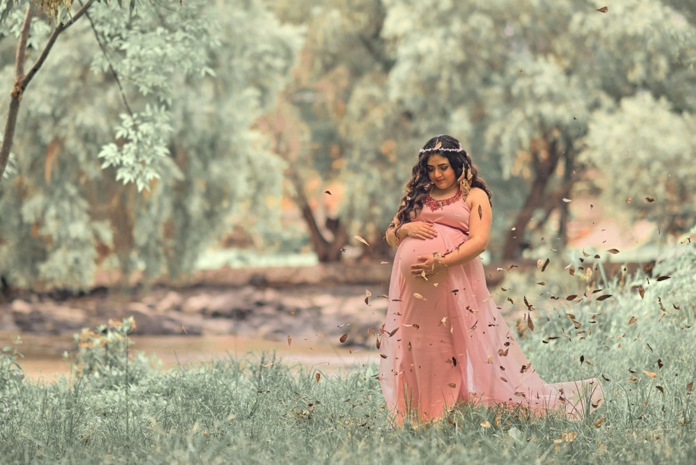 woman holding her pregnant stomach near tree